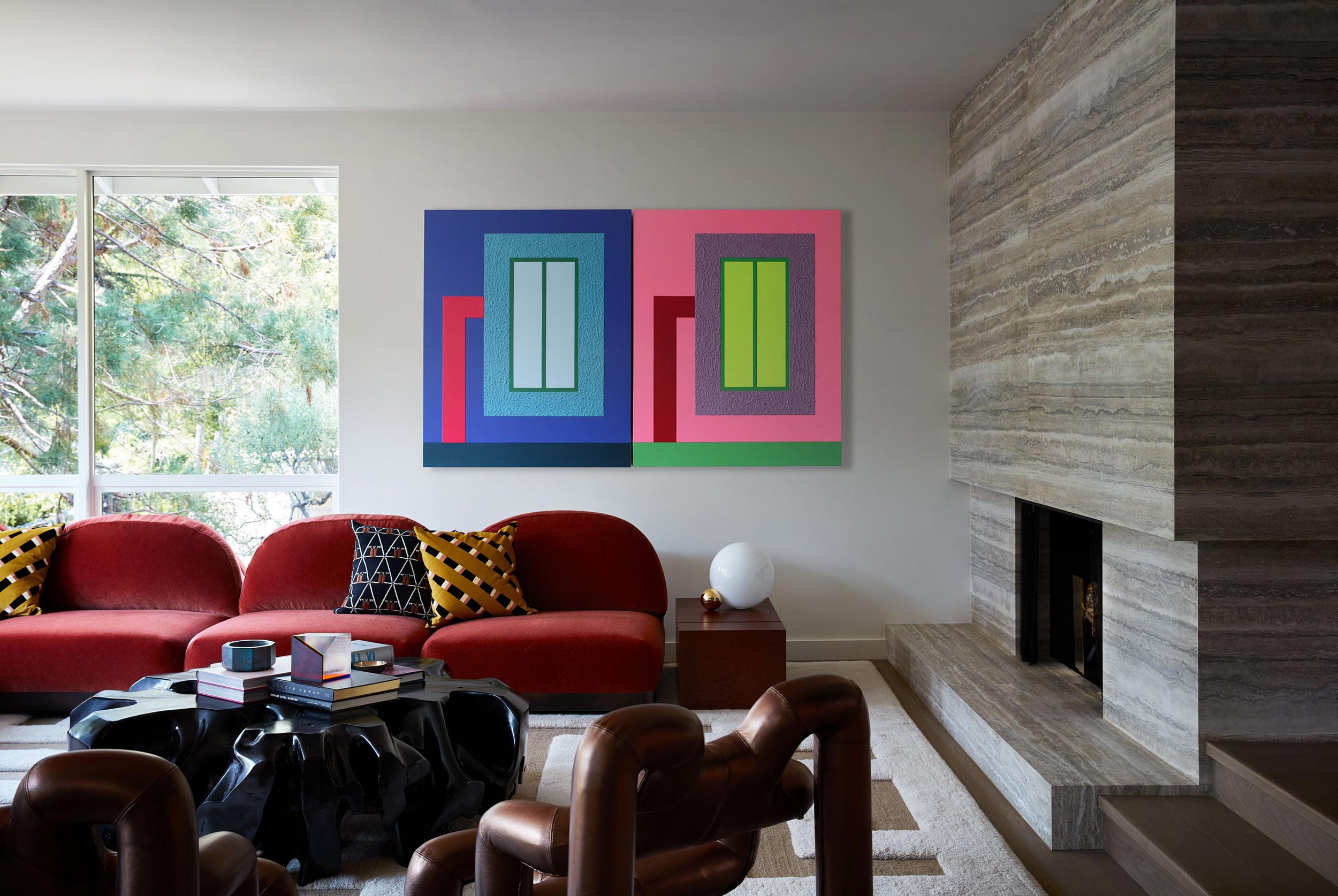 Mid-century modern living room with sculptural red velvet sofa, modern artwork, vintage chairs and fireplace.