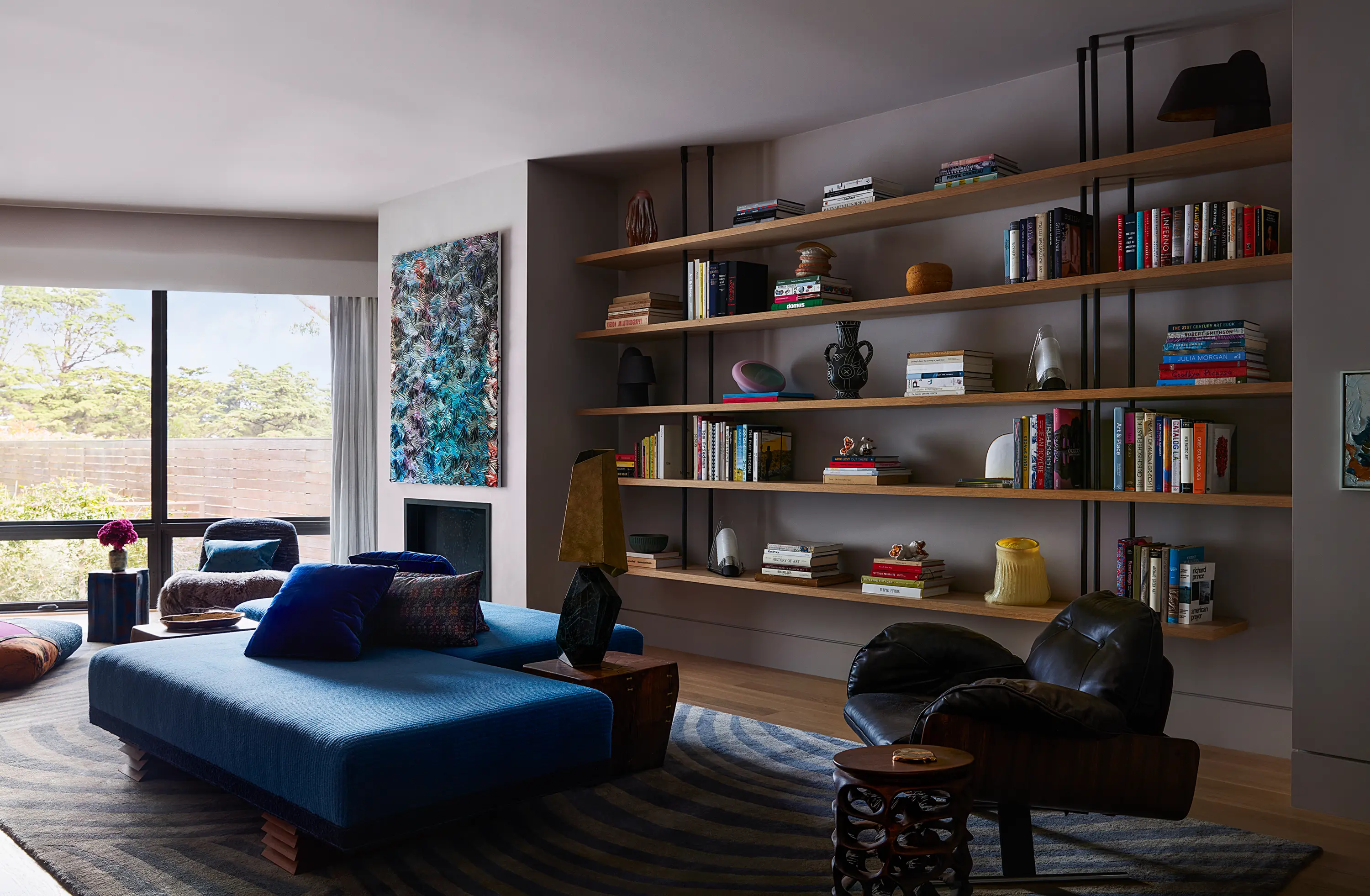 Blue velvet daybeds sits next to a library and abstract painting.