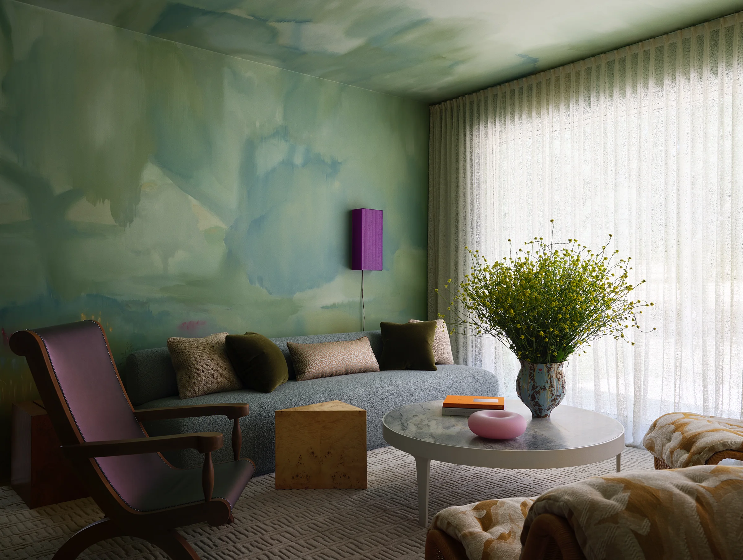 Custom mural by artist frames a velvet sofa with textural pillows, vintage chair, and cork furnishings beneath flowing curtains in serene Sonoma living room.